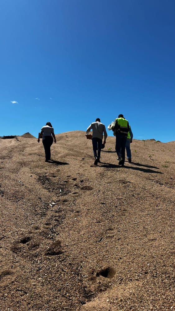 Equipe da Areal Fox subindo uma duna de areia com coletes de segurança, céu azul ao fundo
